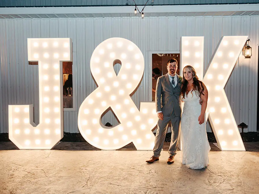 Bride and groom posing with illuminated J&K marquee letters Forest Hills TN at an outdoor wedding