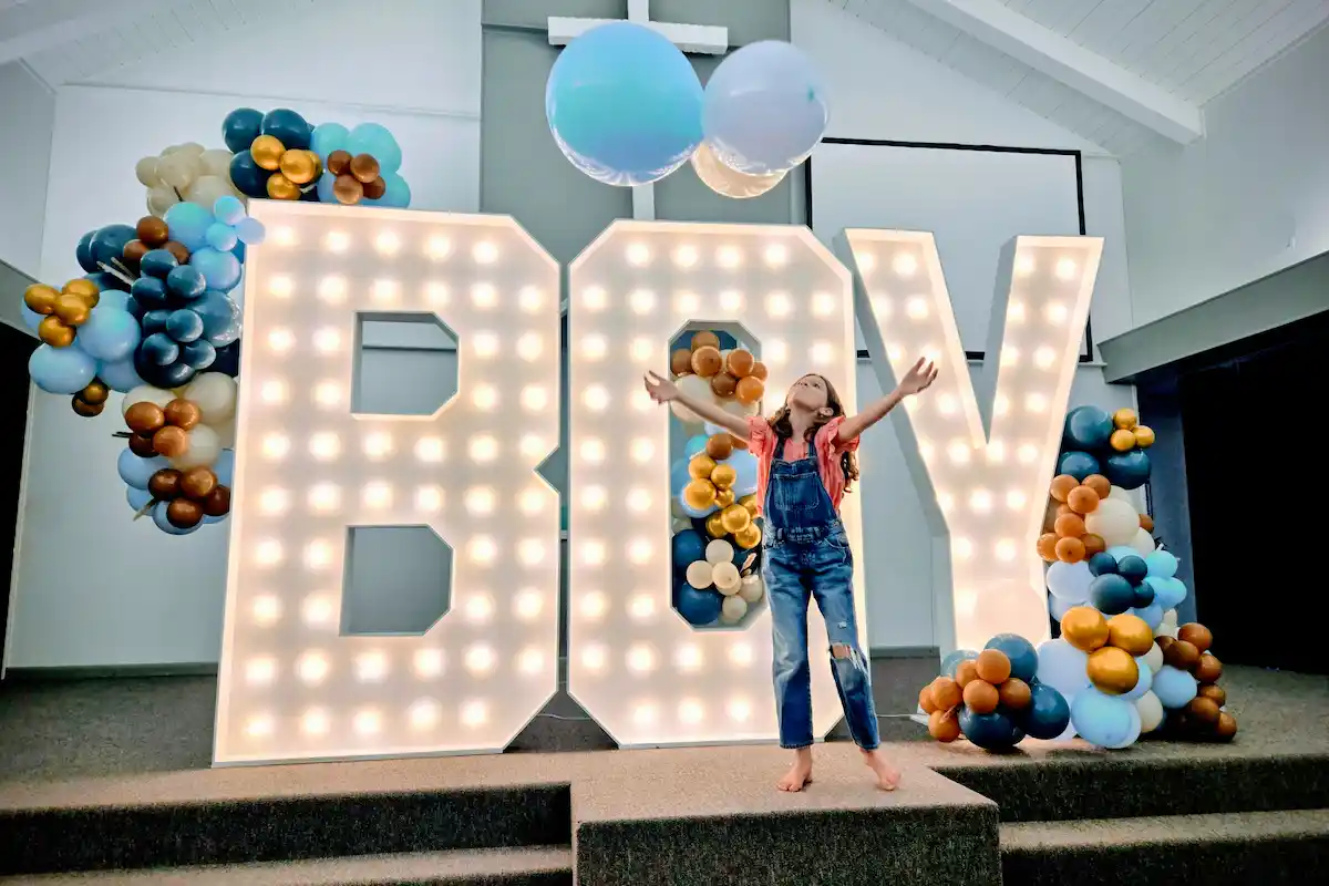 Girl throwing balloon in front of BOY baby shower marquee letters