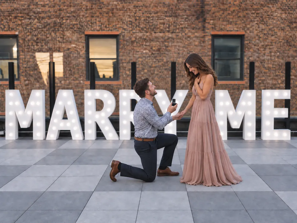 Man on one knee proposing in front of straight-line 4ft MARRY ME letters at a Murfreesboro restaurant