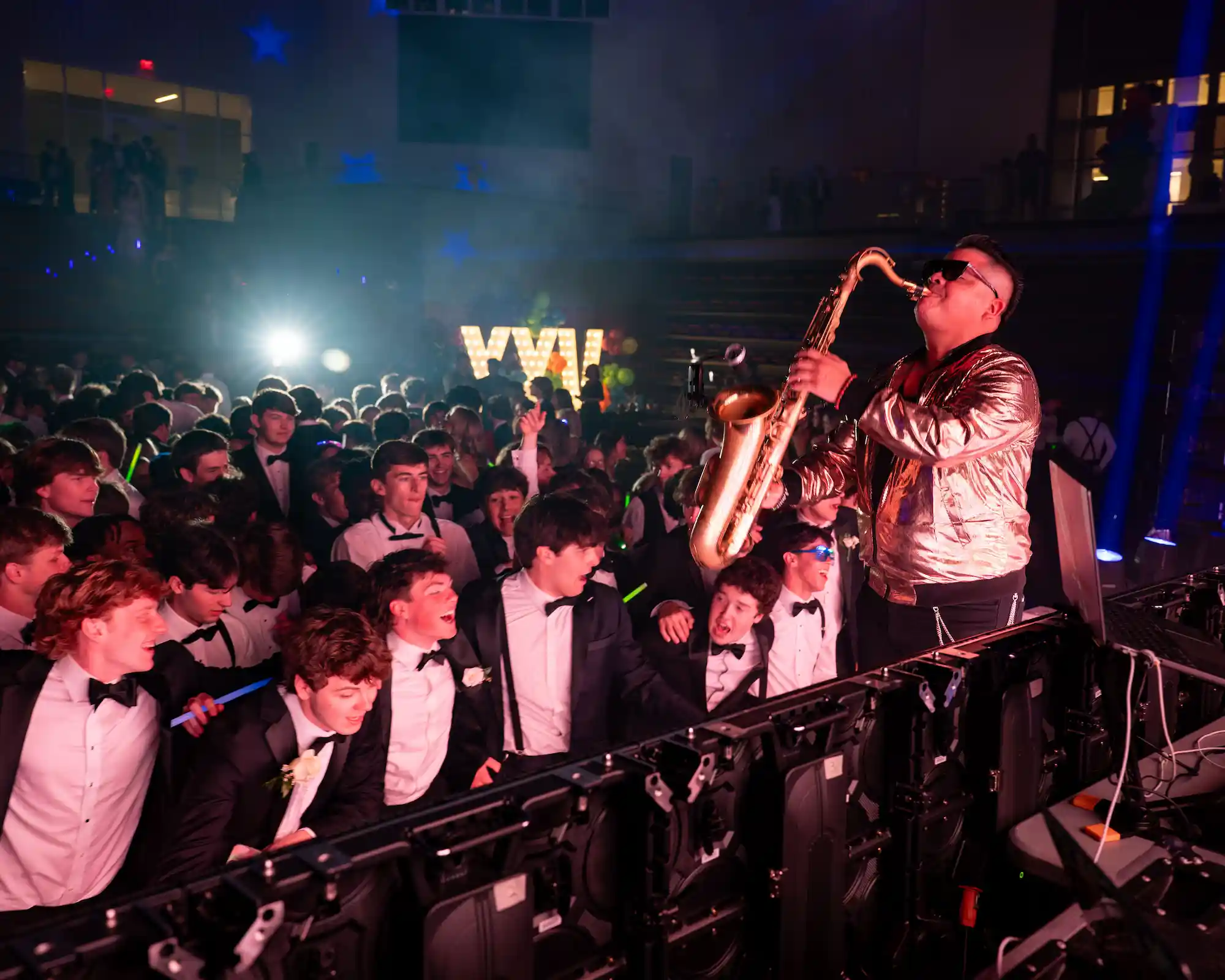 Saxophone player performing on stage at prom with smoke effects and illuminated XXV marquee letters glowing in the background
